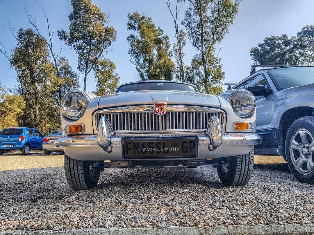 A silver classic MG photographed head-on on gravel.