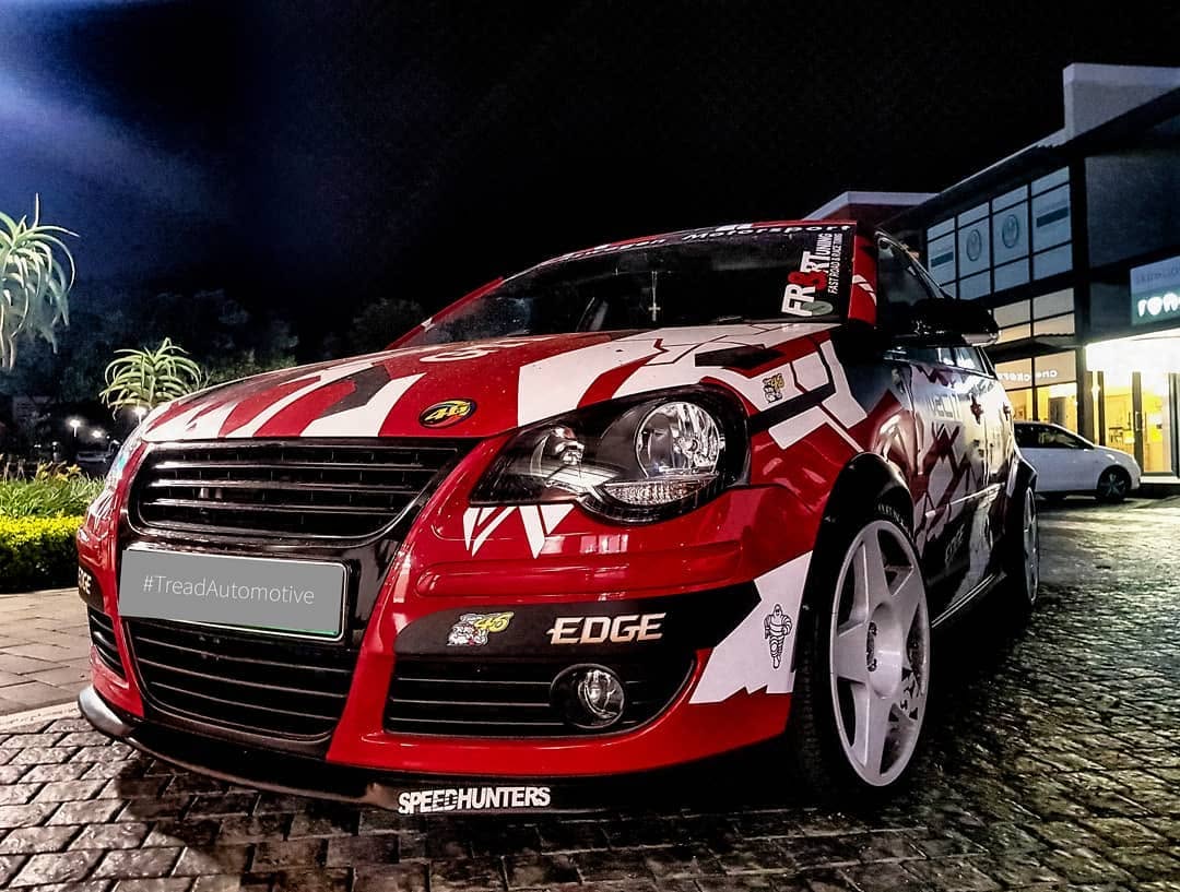 A red and white liveried Volkswagen Polo track car, shot low at night.